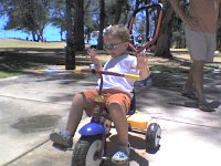 ATT00051  Sammy riding his bike at the beach park. He's gotten pedaling and steering down well enough he toured all around the park and didn't want to turn around to go home!  Here he's pulling tricks already  - no hands!